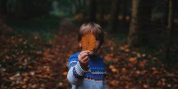 boy holding brown leaf covering his face