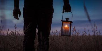 silhouette photo of man carrying candle lantern with lighted candle