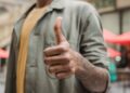 Crop faceless young black male in casual outfit standing on city street and showing thumb up gesture