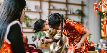 A family gathering for Chinese New Year, exchanging red envelopes and wearing traditional attire indoors.
