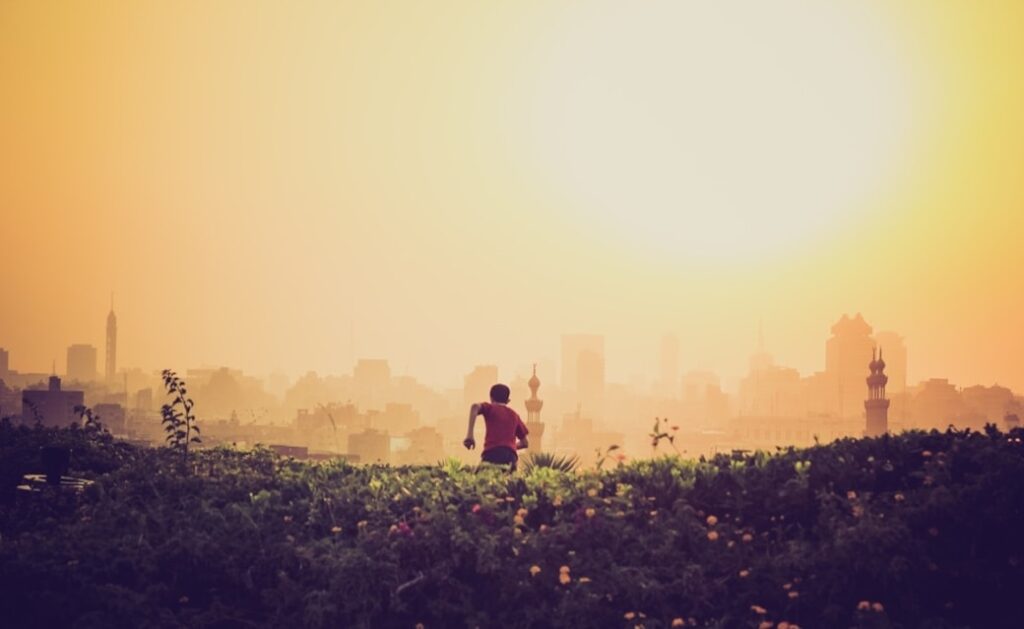 man running towards the city on green grass field during golden time