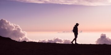silhouette of person walking under white clouds