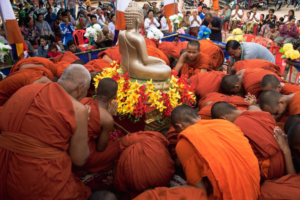 Monks in orange robes conduct a religious ceremony around a golden Buddha statue outdoors.